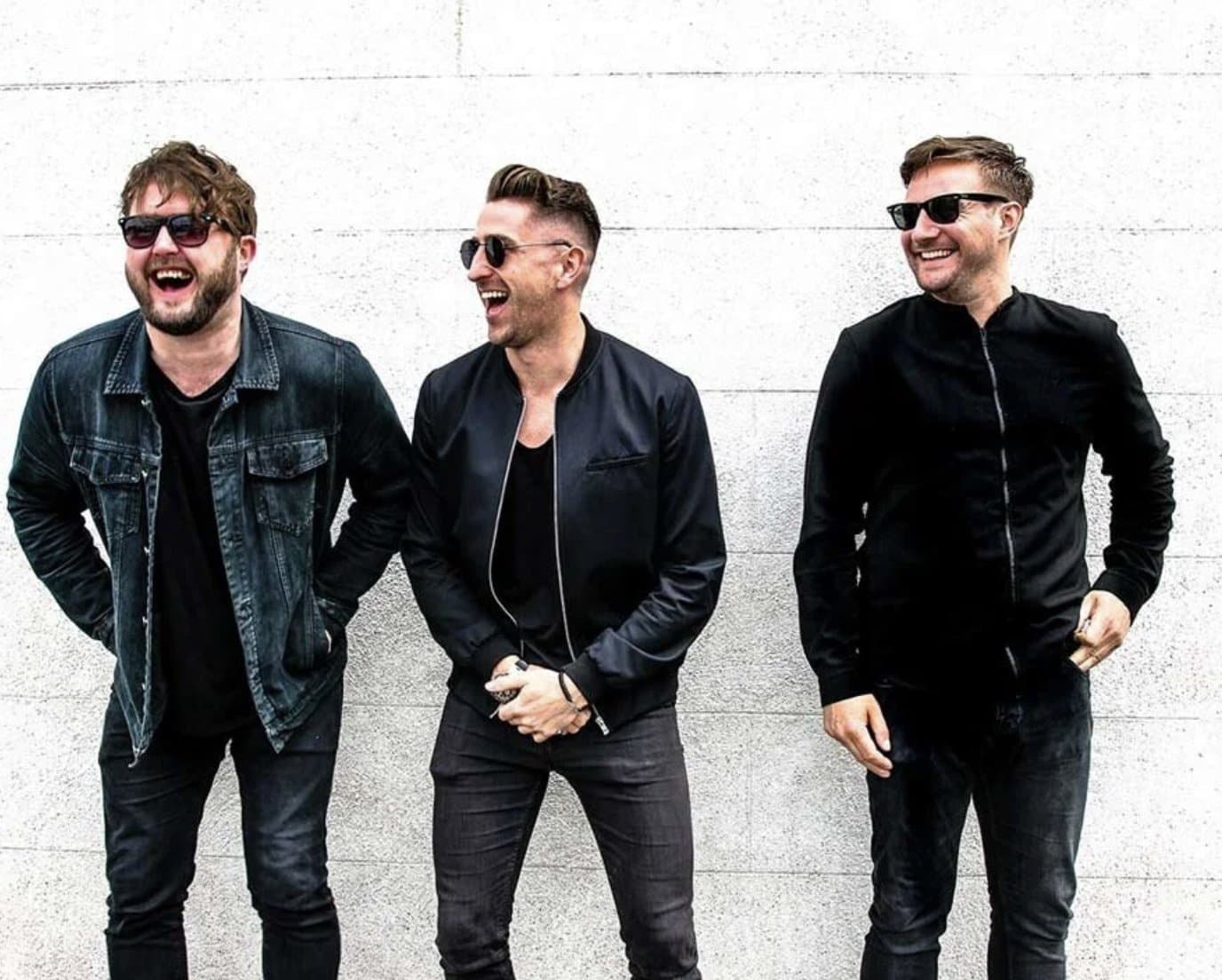 A live band photographed together against a plain wall.