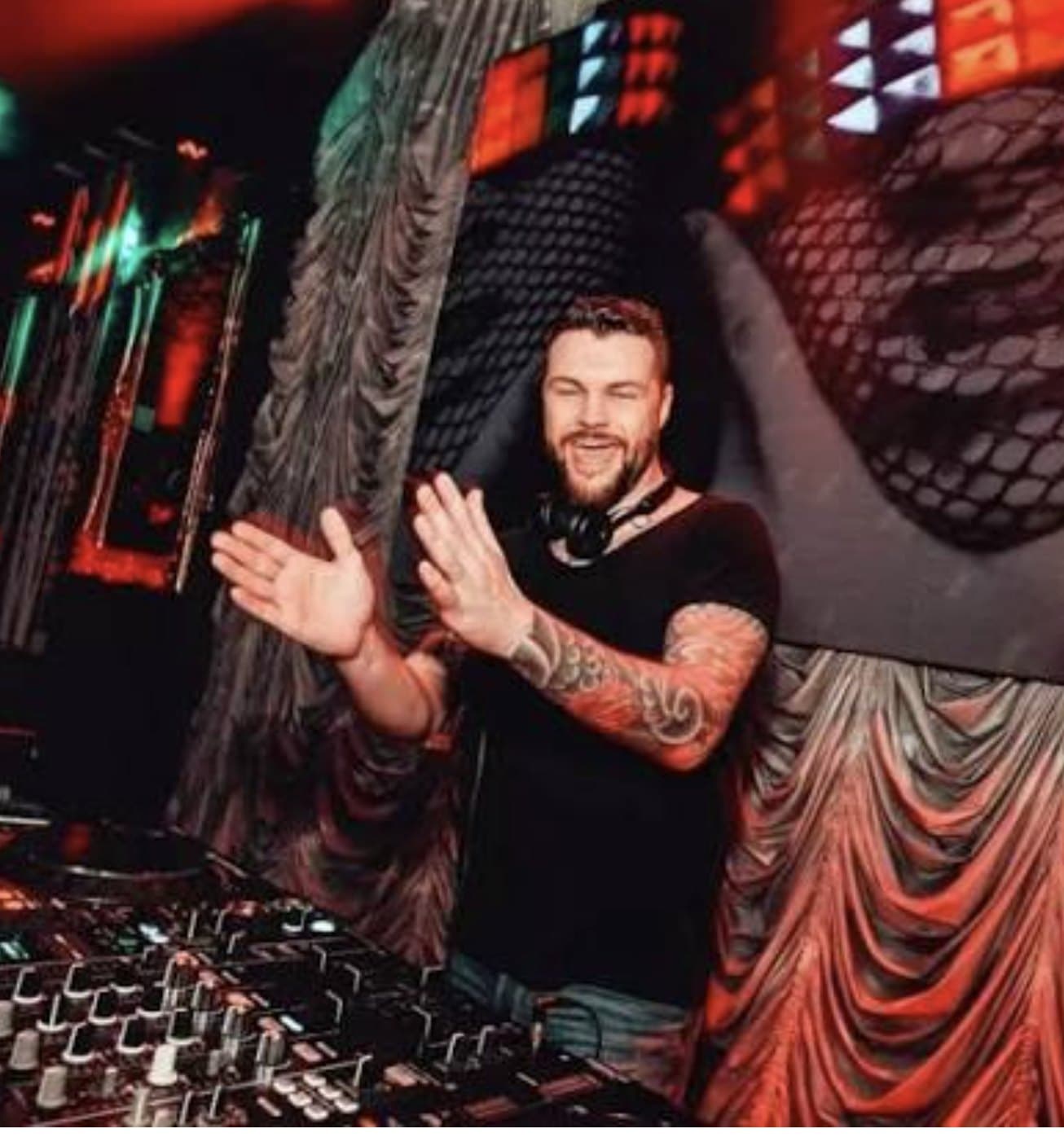 A DJ up out of the booth, hands together, mid-set.