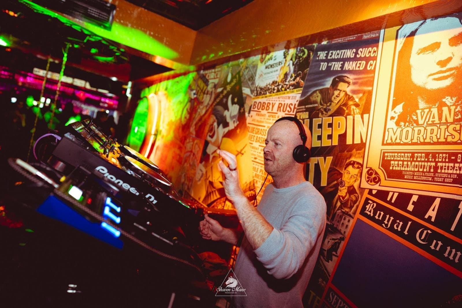 A DJ at the decks with the room behind.