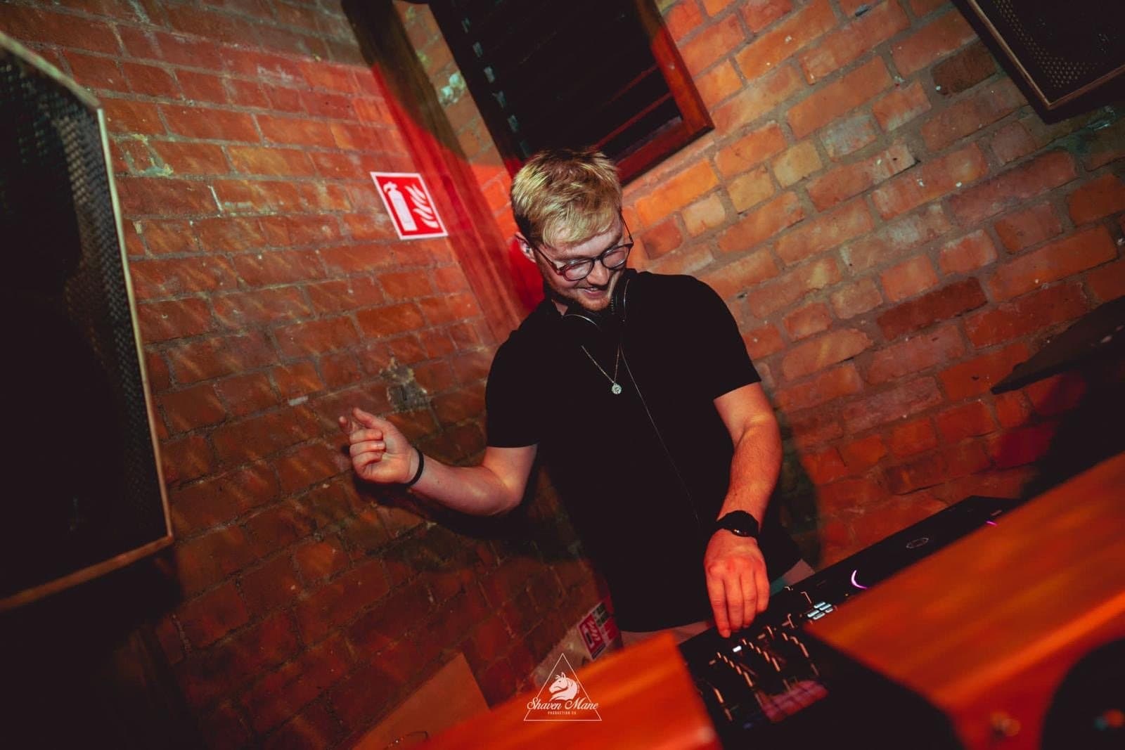 A DJ at the decks against bare brick in red light.