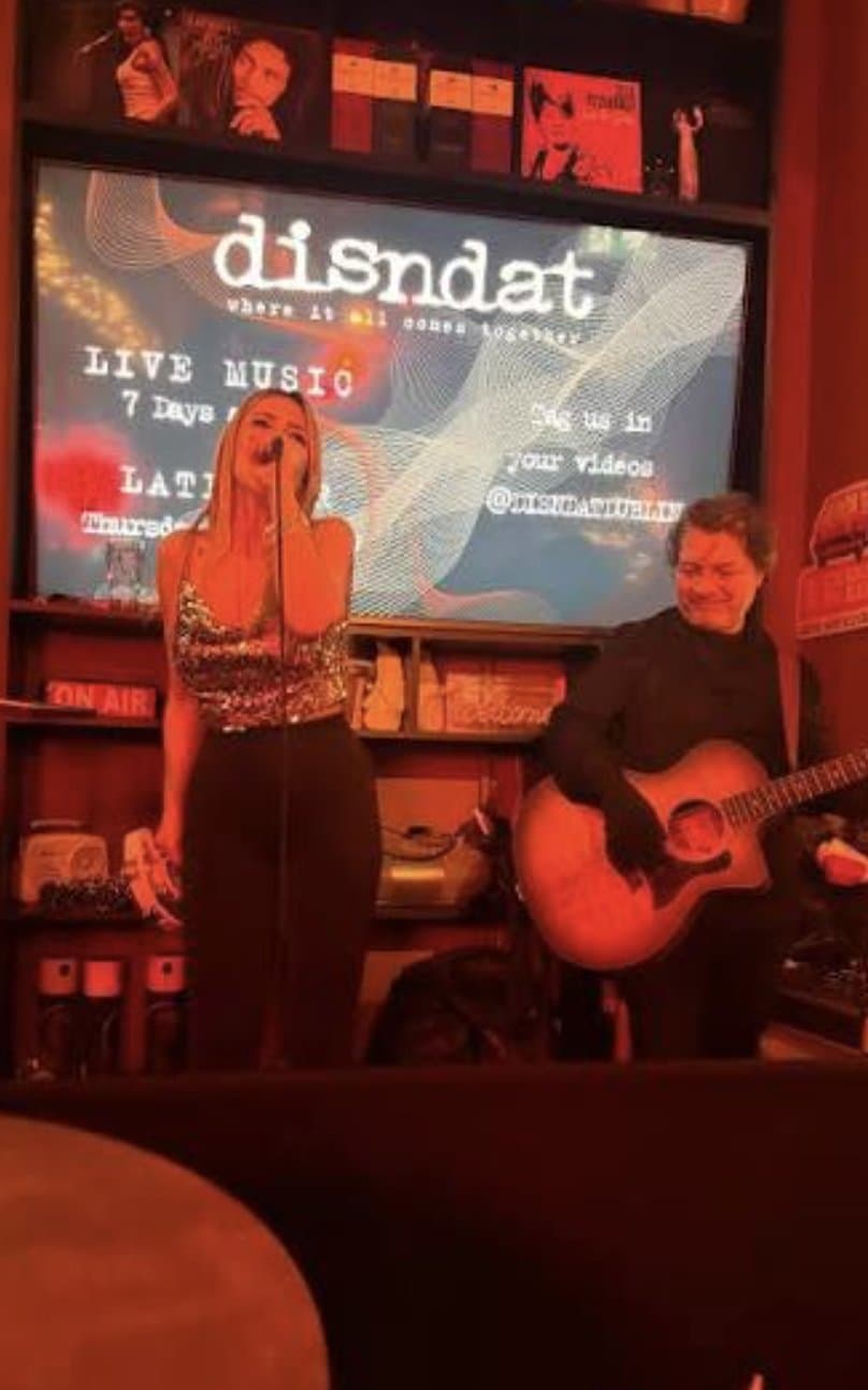 A singer and guitarist performing together in a bar.