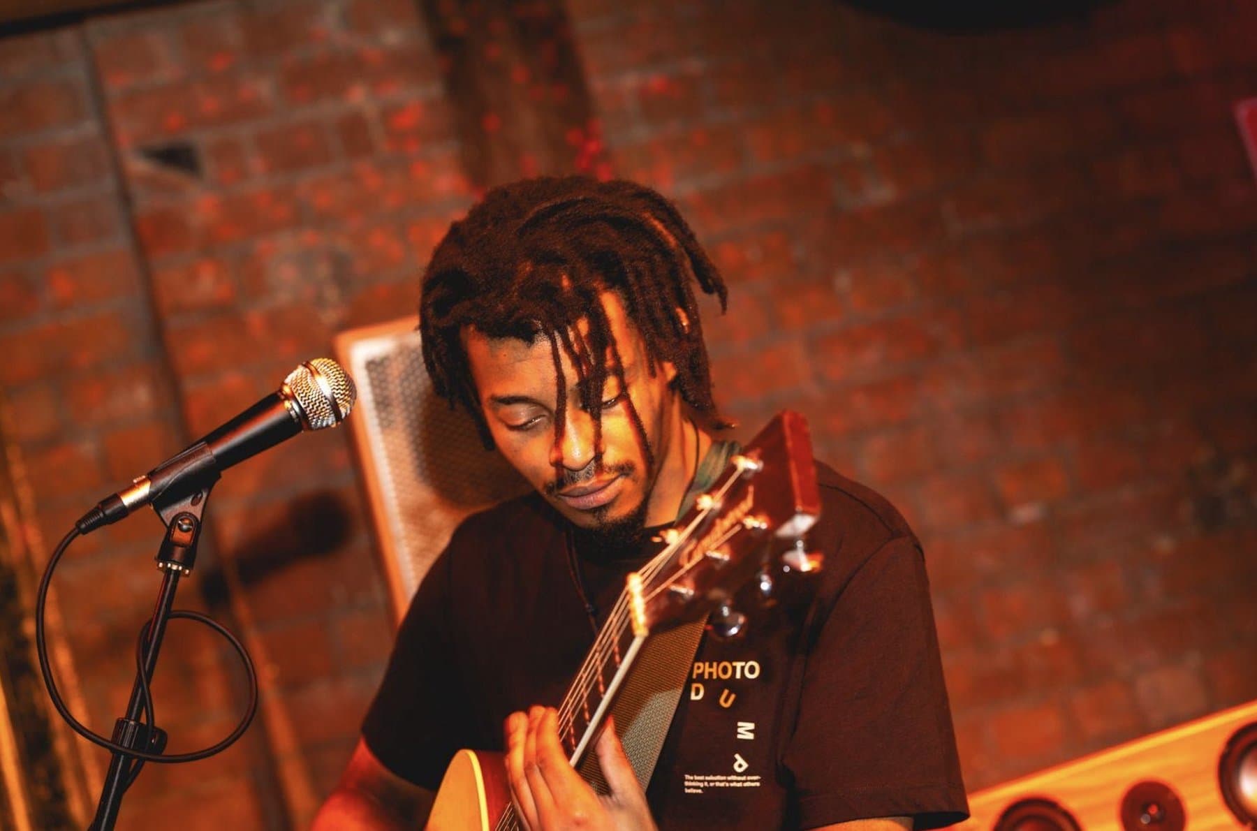 A guitarist playing close to the crowd against a brick wall.