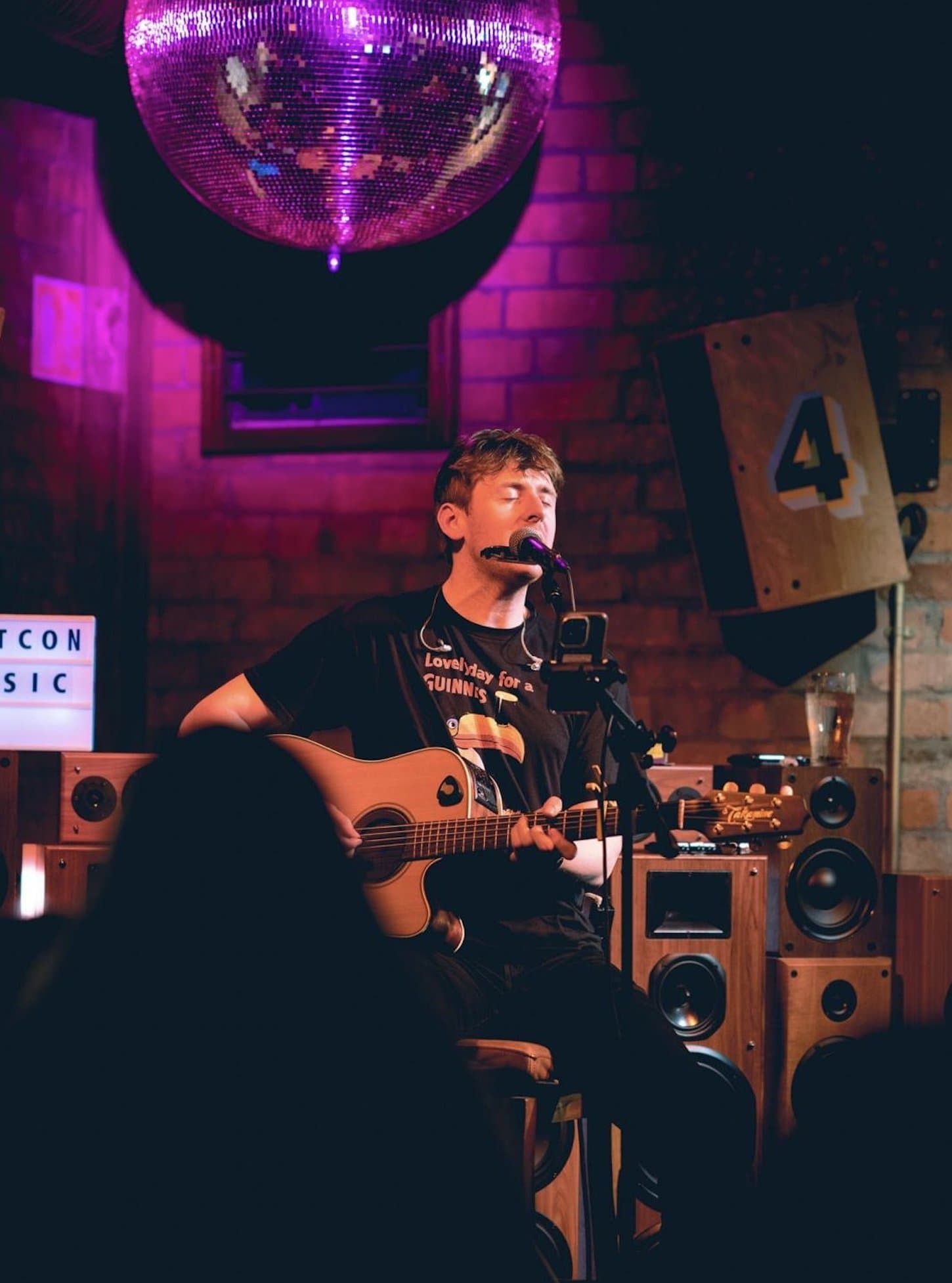 A guitarist singing and playing seated under a mirrorball.